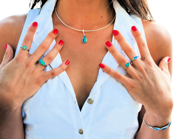 A model wearing a white shirt with bright red fingernails wears opal rings, bracelet and pendant by Black Star Opal