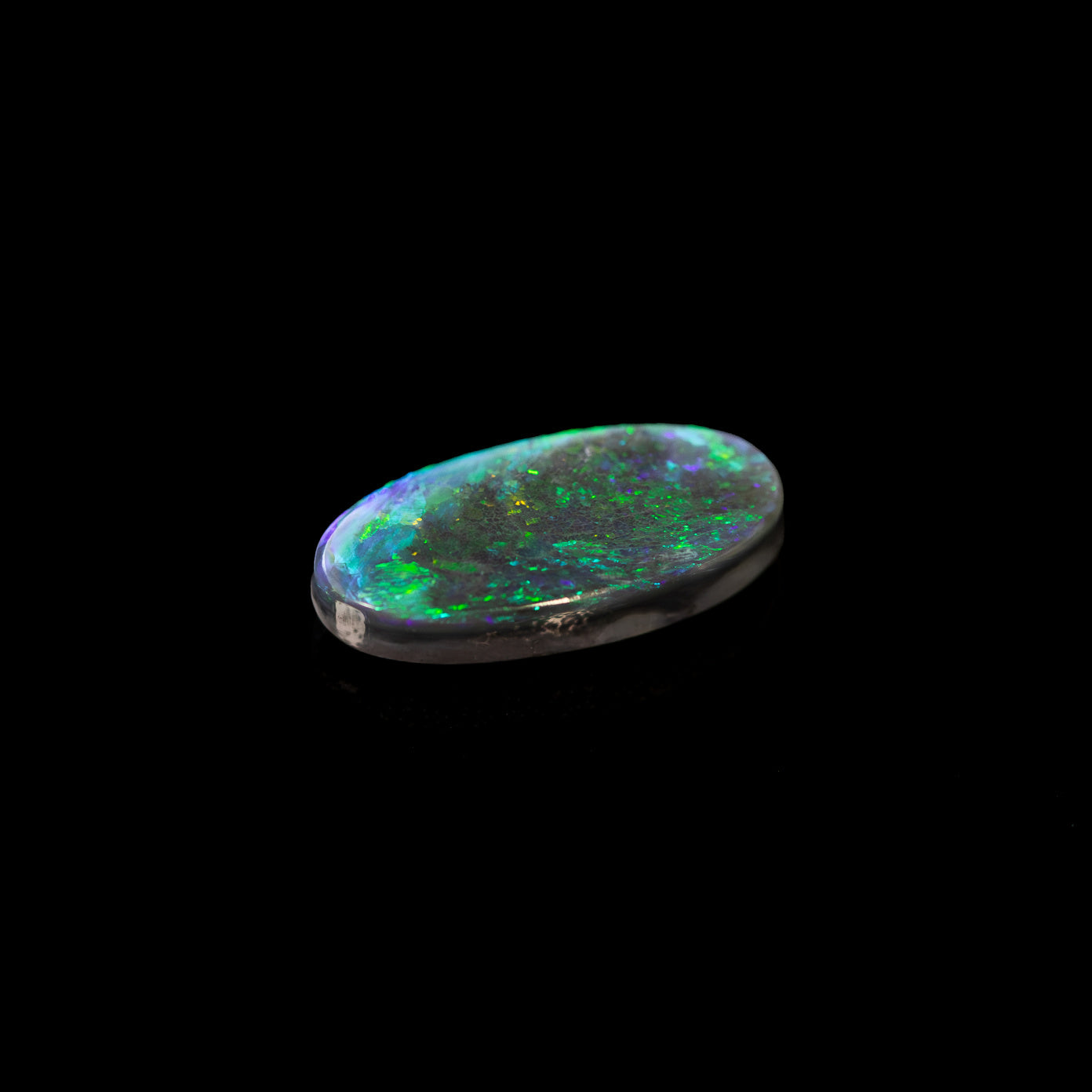Oval black opal with dark body tone and striking green flashes, ethically sourced in Australia