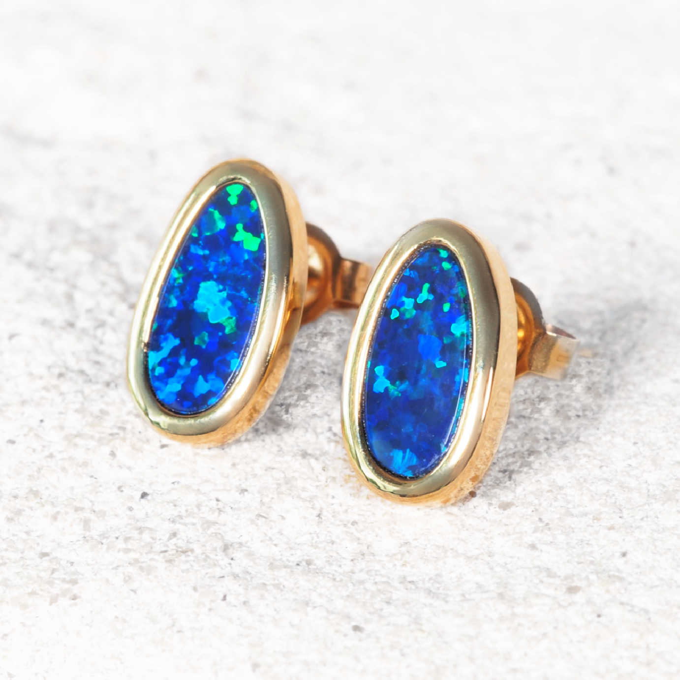 Gold earrings with blue opal stones on a textured white background