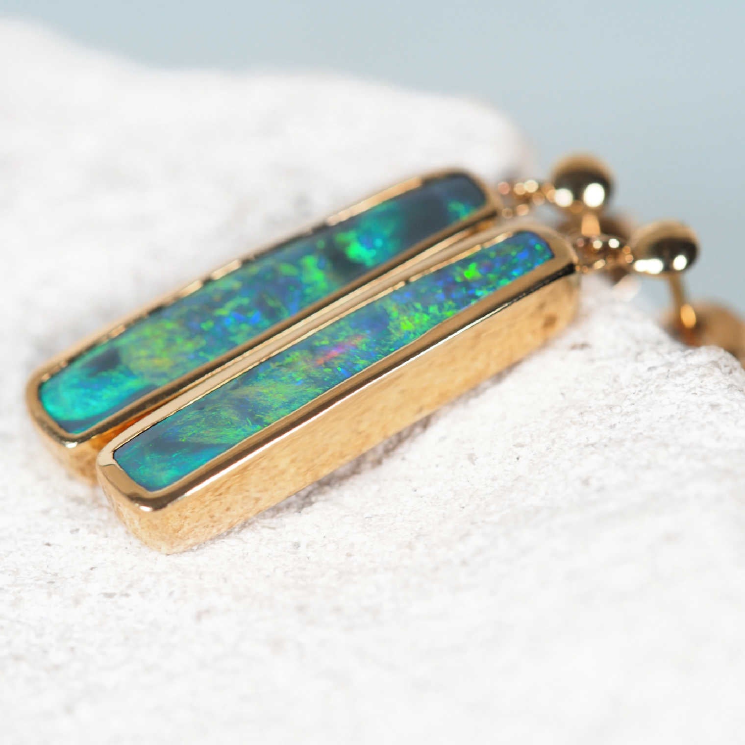 Close-up of 'Margareta' solid black opal earrings bezel set in yellow gold, highlighting vibrant multi-coloured play-of-colour.