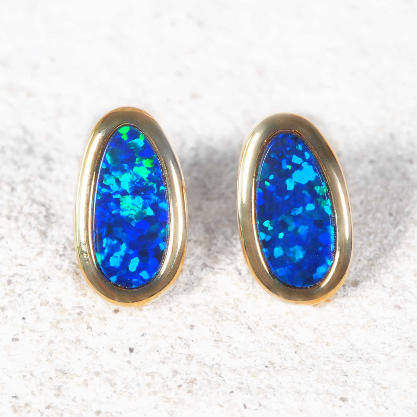 Pair of blue opal earrings with gold settings on a textured white surface