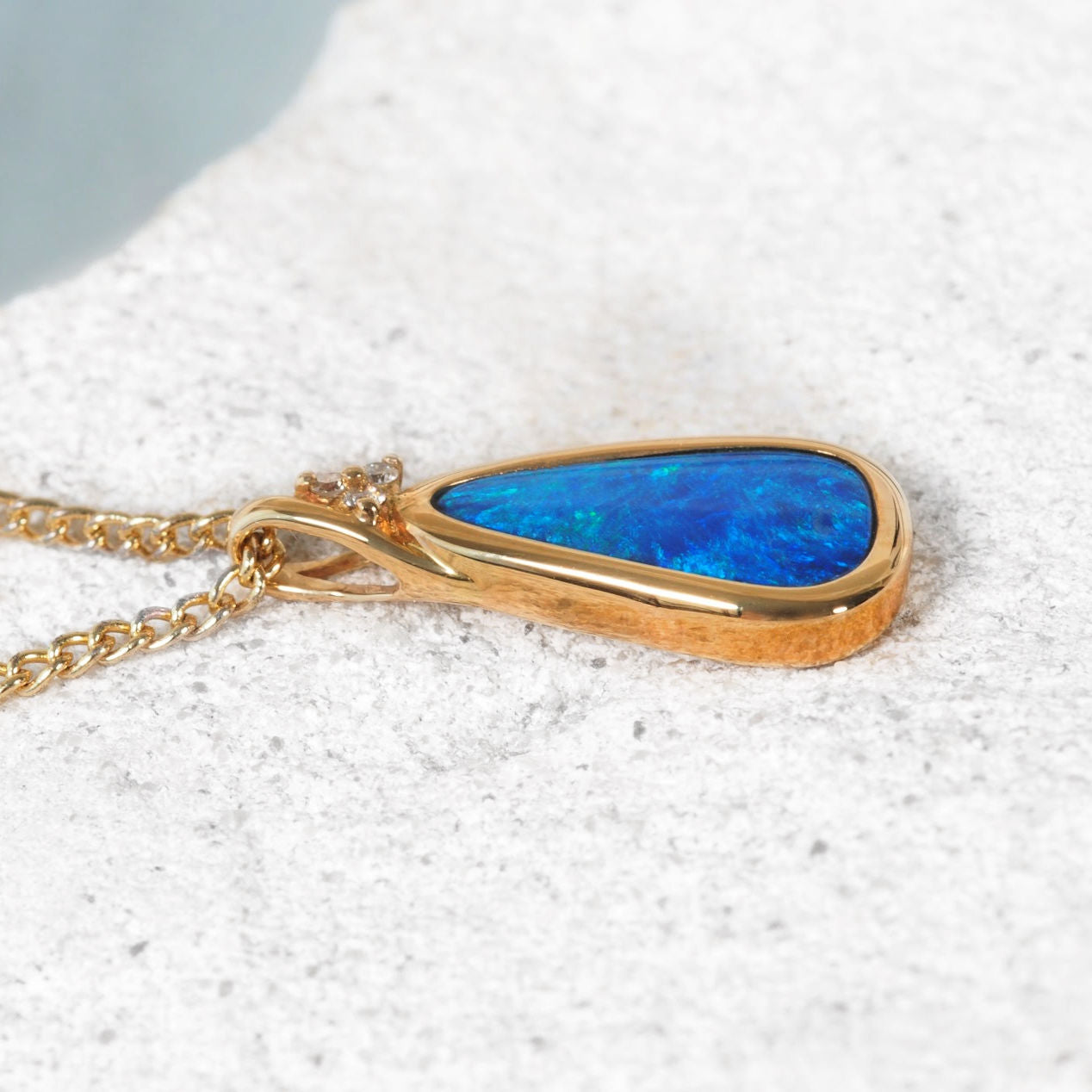 Gold necklace with a blue opal gemstone on a textured white surface