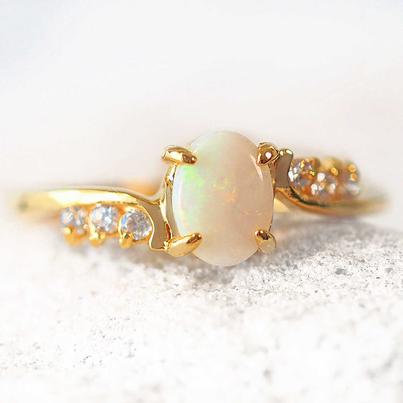 Gold ring with a central opal stone and smaller crystals on a white background