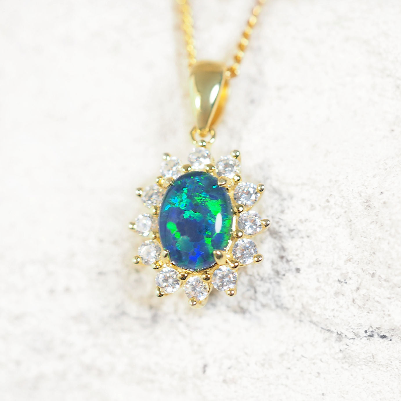 'Princess Blue' opal pendant in polished gold-plated silver with claw-set oval Australian triplet opal and halo of 12 cubic zirconias
