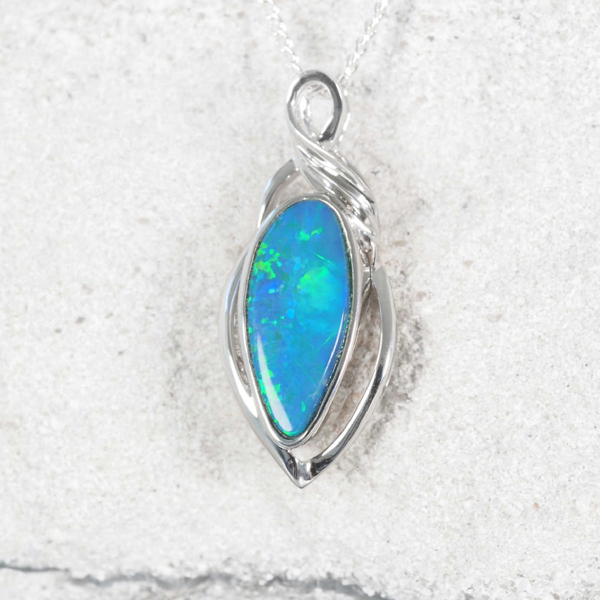 A silver Australian opal pendant featuring a teardrop-shaped blue and green opal gemstone, displayed on a textured white stone surface.