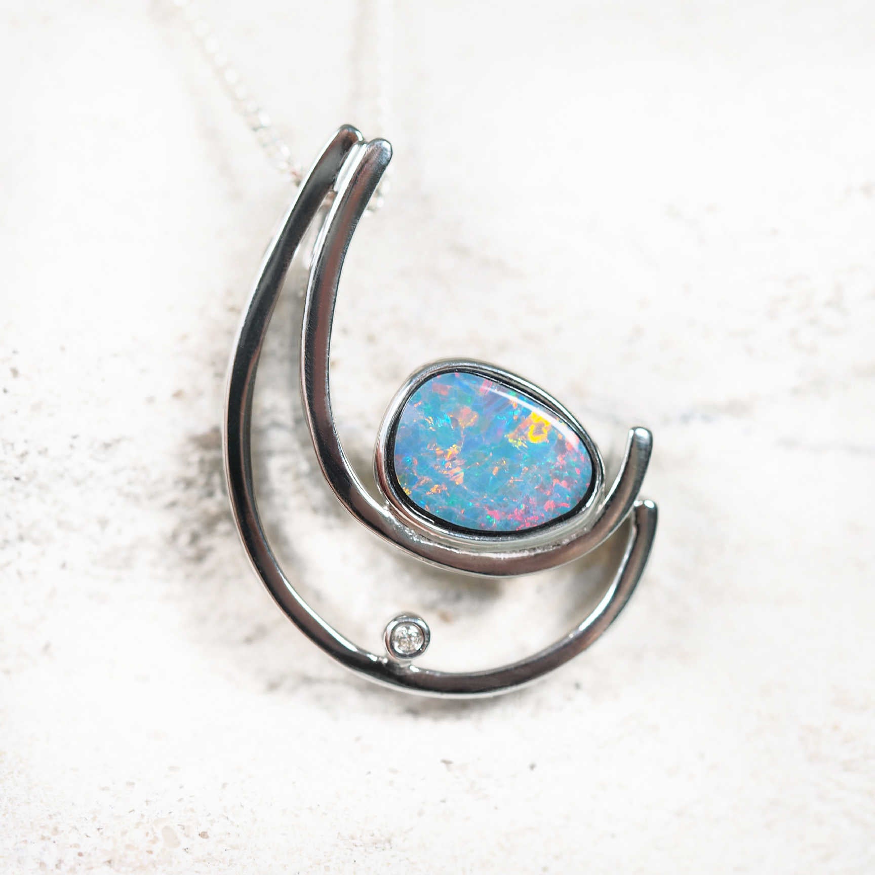 Sterling silver curved opal pendant featuring a vibrant multi-coloured freeform Australian doublet opal with a sparkling crystal accent.