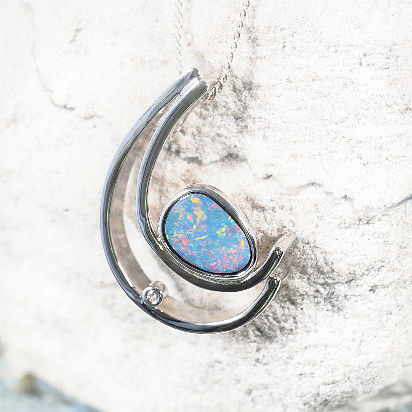 Contemporary silver opal pendant with a curved design, showcasing a bezel-set multi-coloured Australian doublet opal and a sparkling crystal detail.