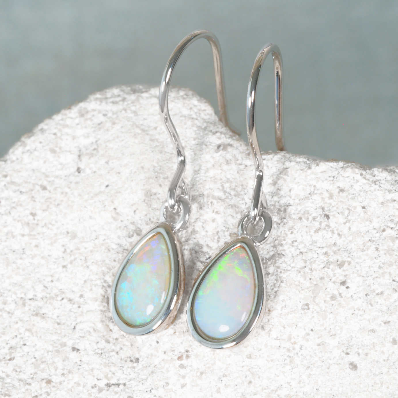 Opal earrings on a textured surface with a neutral background