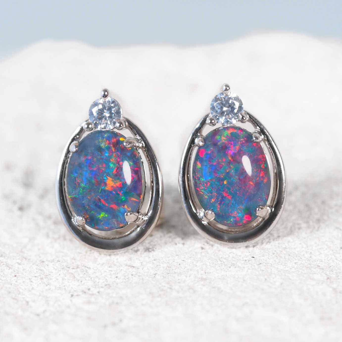 Pair of opal earrings with silver setting on a textured surface