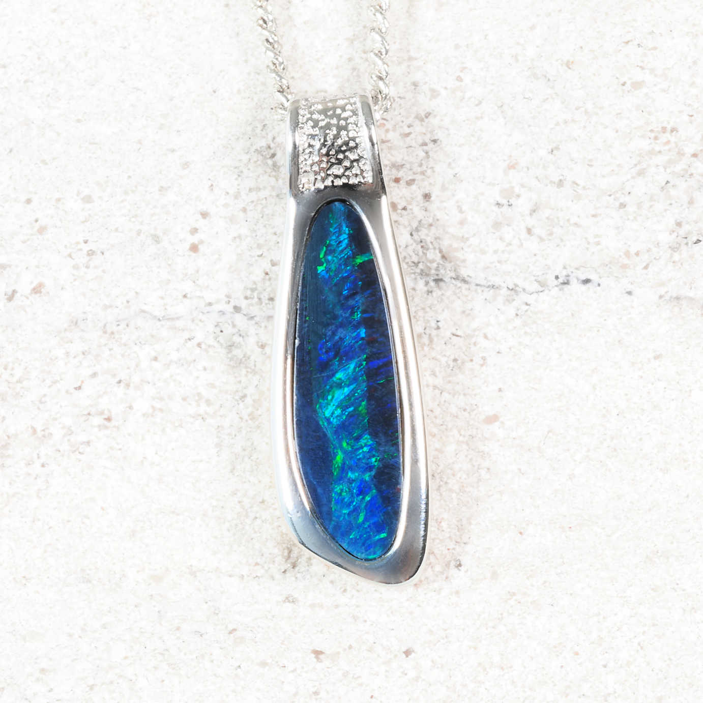Blue opal pendant with silver setting on a textured white surface