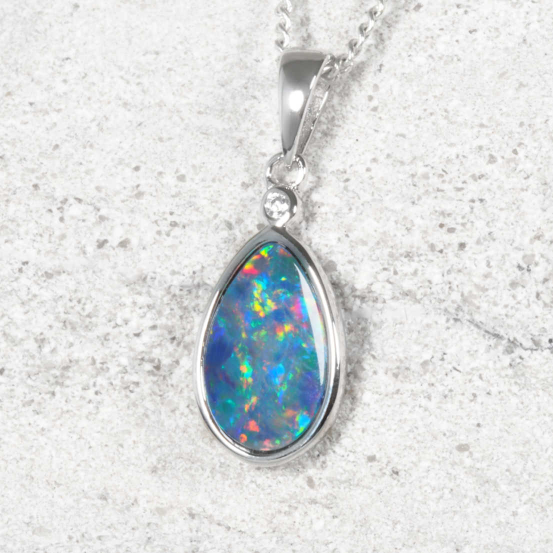 A silver teardrop Australian opal pendant necklace featuring a vibrant, multicolored opal gemstone and a small clear accent stone.