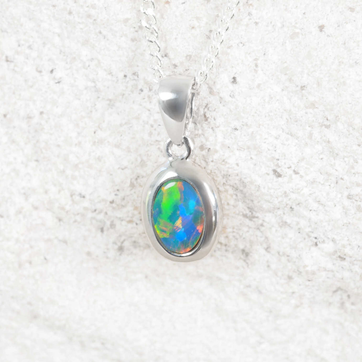 A 14ct white gold opal pendant necklace featuring an oval-cut opal gemstone with vibrant green, blue, and orange play-of-color, displayed on a textured light gray background.
