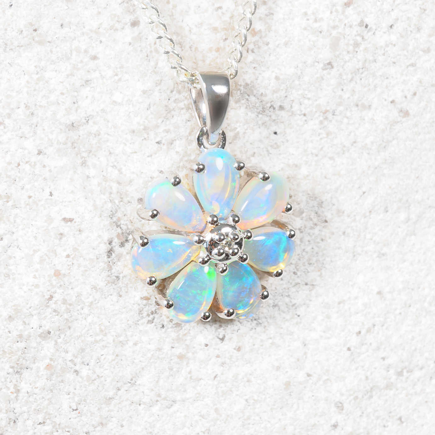 Opal flower pendant on a silver chain against a light gray background
