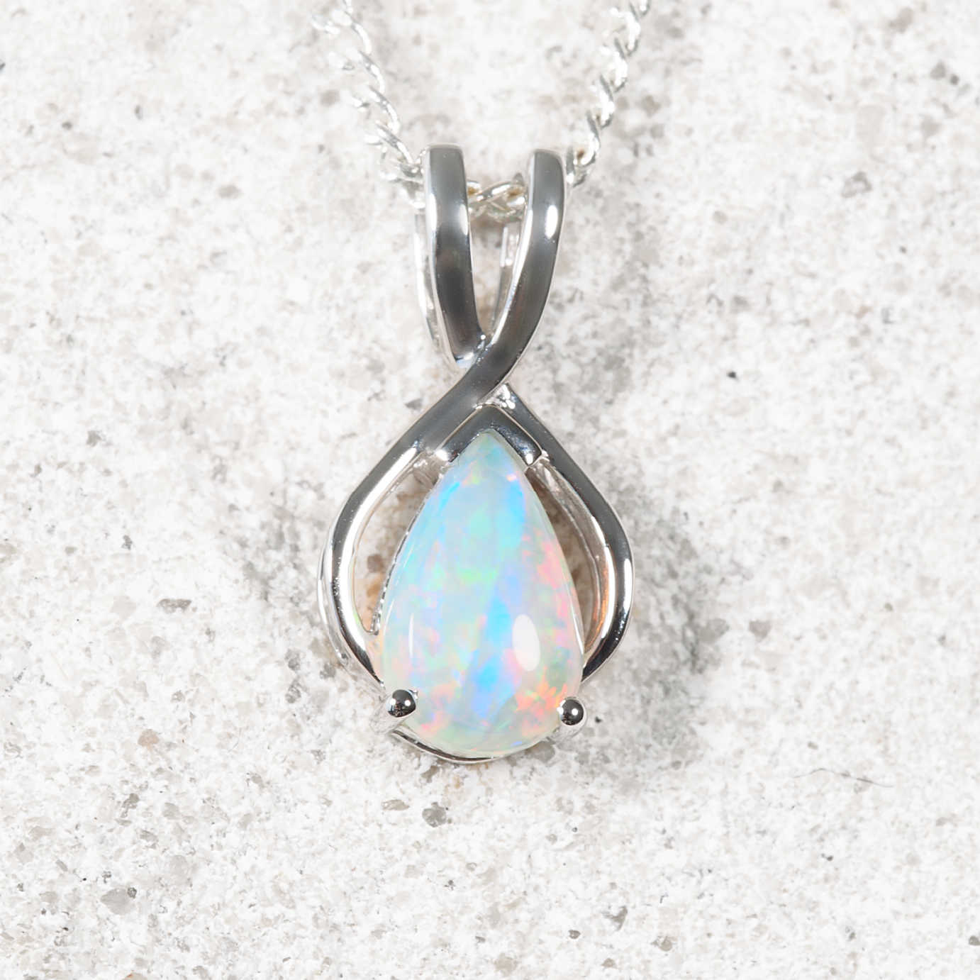 Opal pendant in a white gold setting on a textured white background