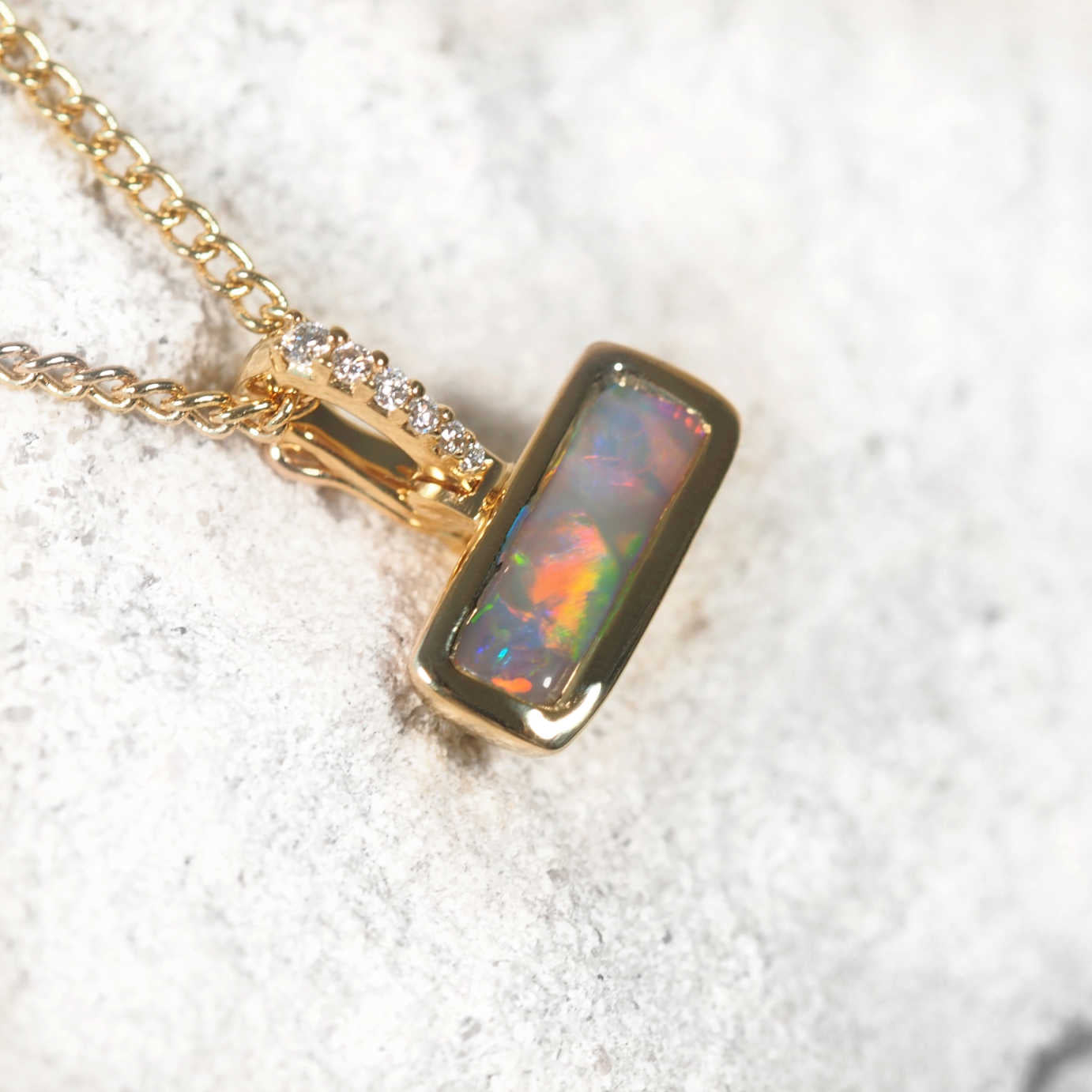 Gold necklace with an opal pendant on a textured white surface