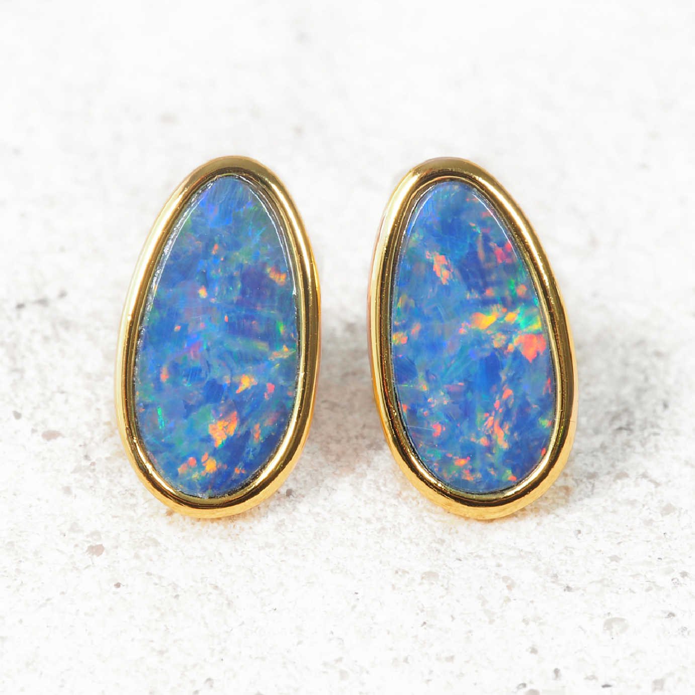 Opal earrings with gold setting on a textured white background