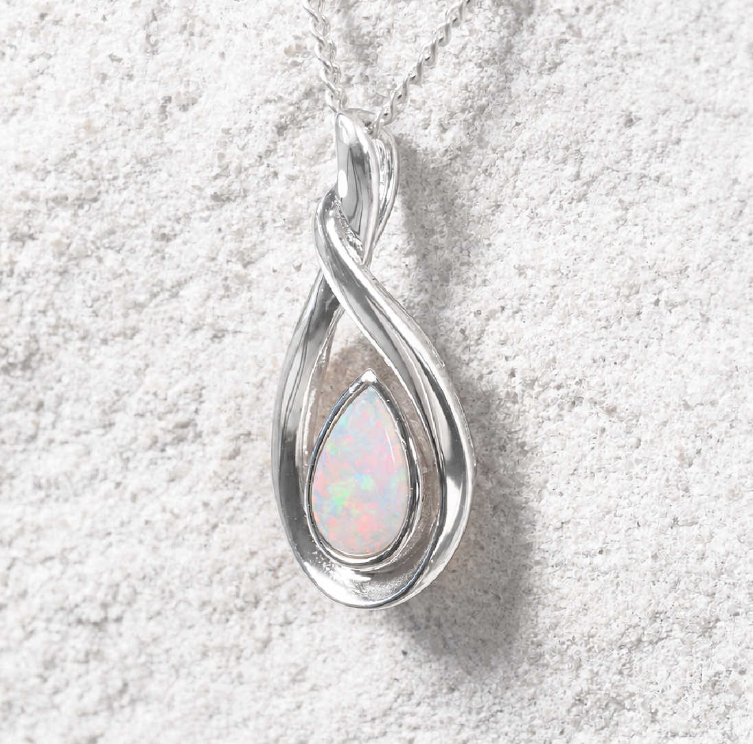 A silver teardrop pendant necklace featuring a swirling twisted design around a teardrop-shaped iridescent opal gemstone, resting on a textured light gray surface.
