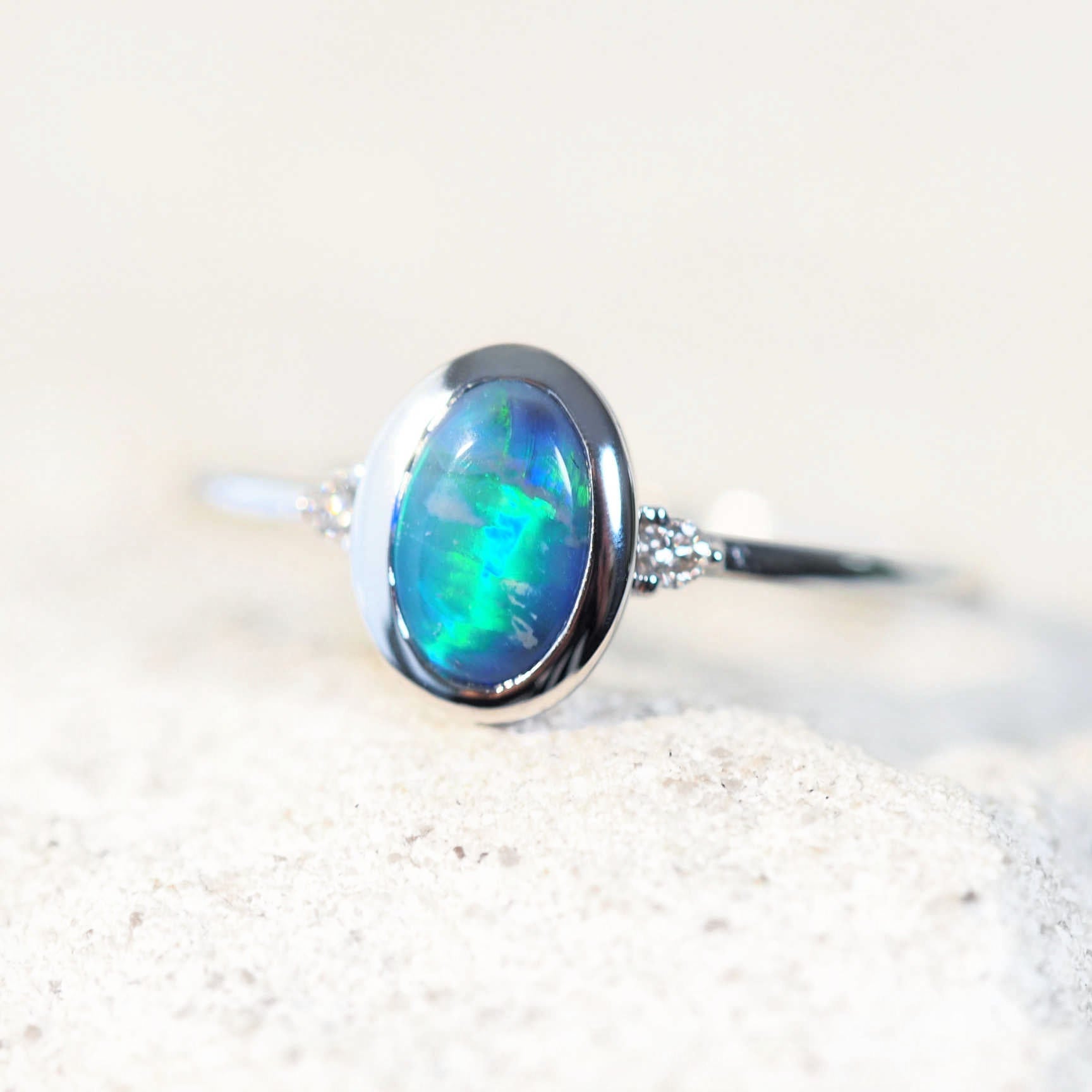 Anneisha handcrafted opal ring with a green Lightning Ridge black opal, bezel-set in 14ct white gold and adorned with two sparkling white diamonds.