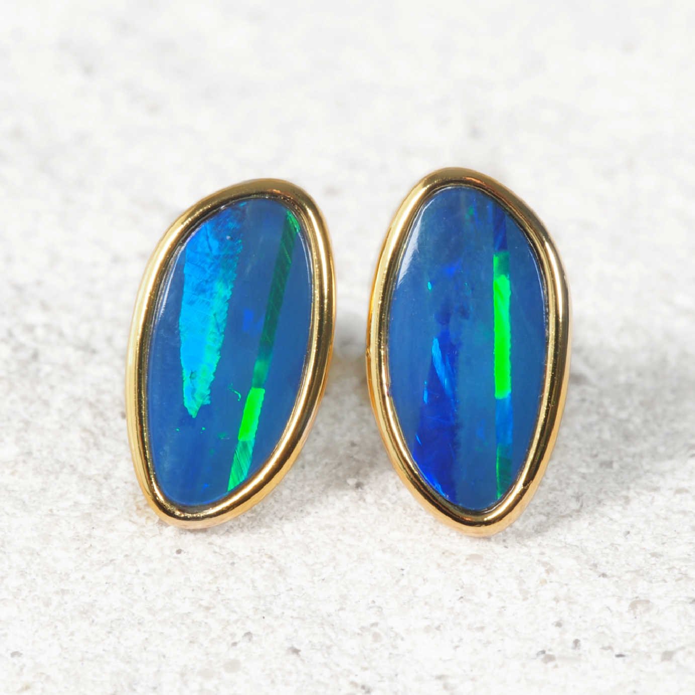 Pair of gold-framed blue opal earrings on a textured white surface
