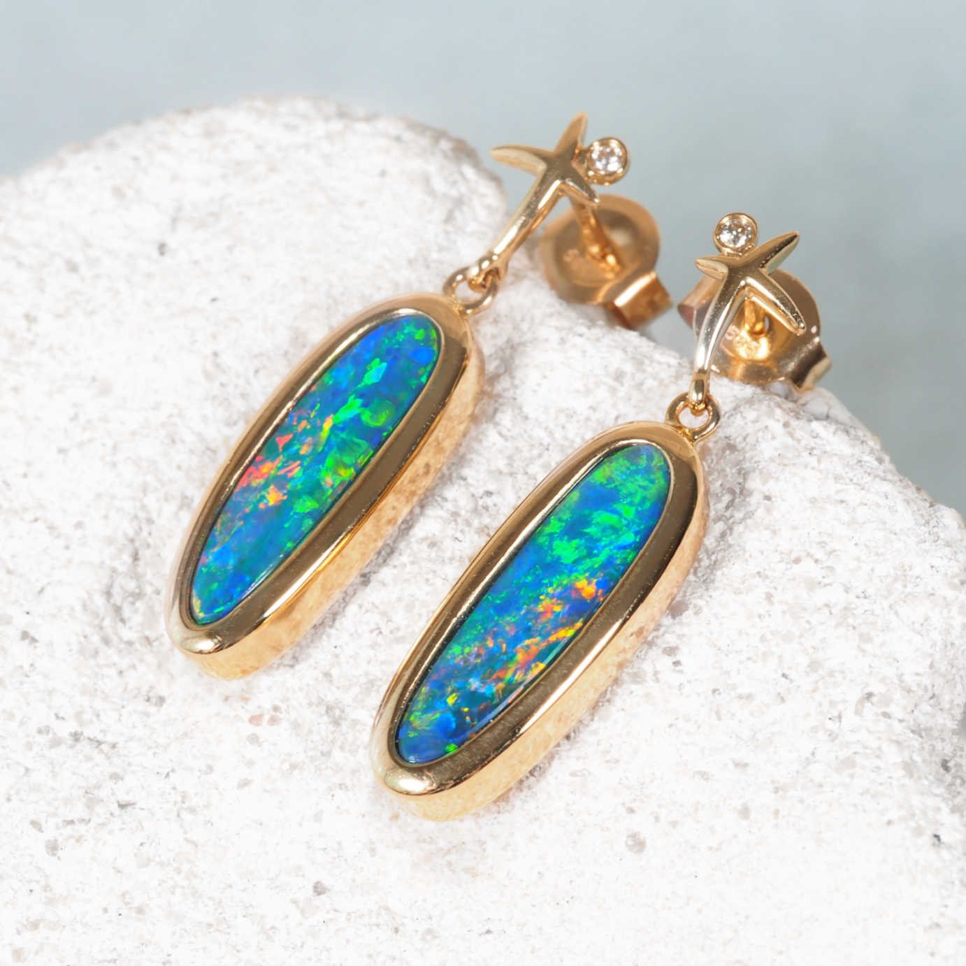 Gold earrings with colorful opal stones on a white surface