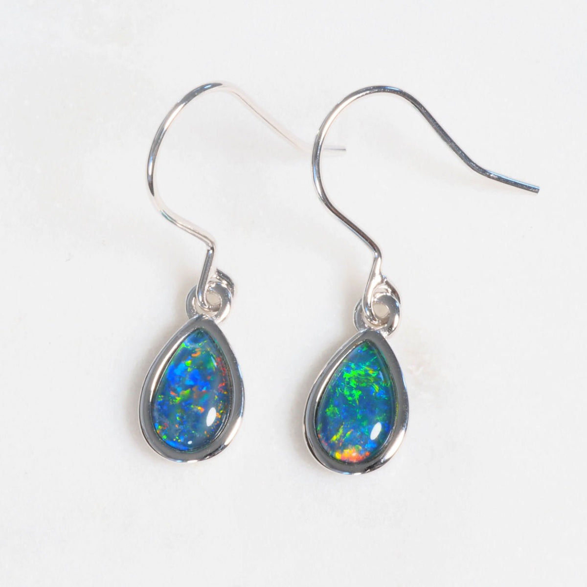 A pair of silver drop opal earrings featuring teardrop-shaped Australian opal gemstones that display vibrant blue, green, and orange flashes, set on silver hook wires against a plain white background.