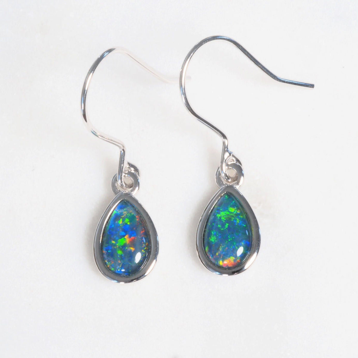 A pair of Australian silver drop opal earrings featuring teardrop-shaped opal stones that display vibrant blue, green, and orange flashes, set in polished silver hooks on a plain white background.