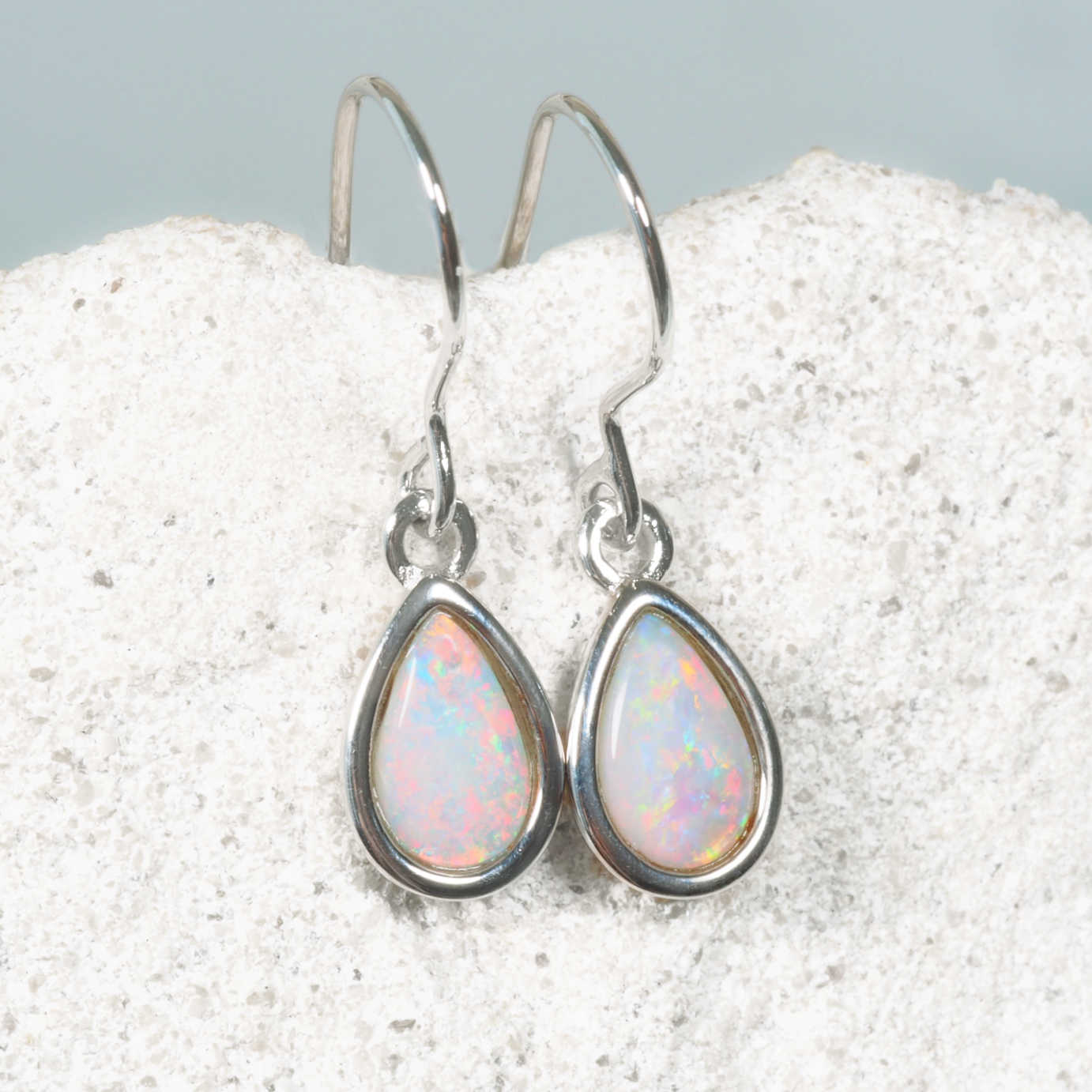 Teardrop-shaped opal earrings on a textured white surface with a light gray background