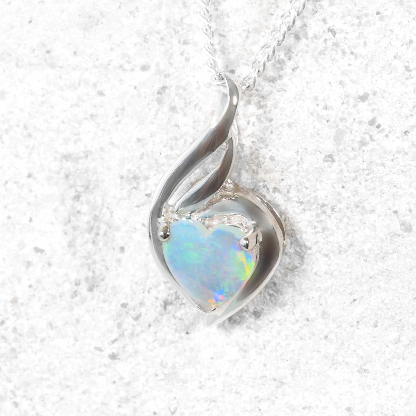 Heart-shaped opal pendant in a white gold setting on a textured white background
