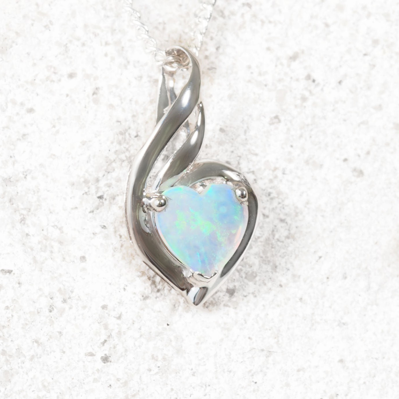 Heart-shaped opal pendant in silver setting on a textured white background
