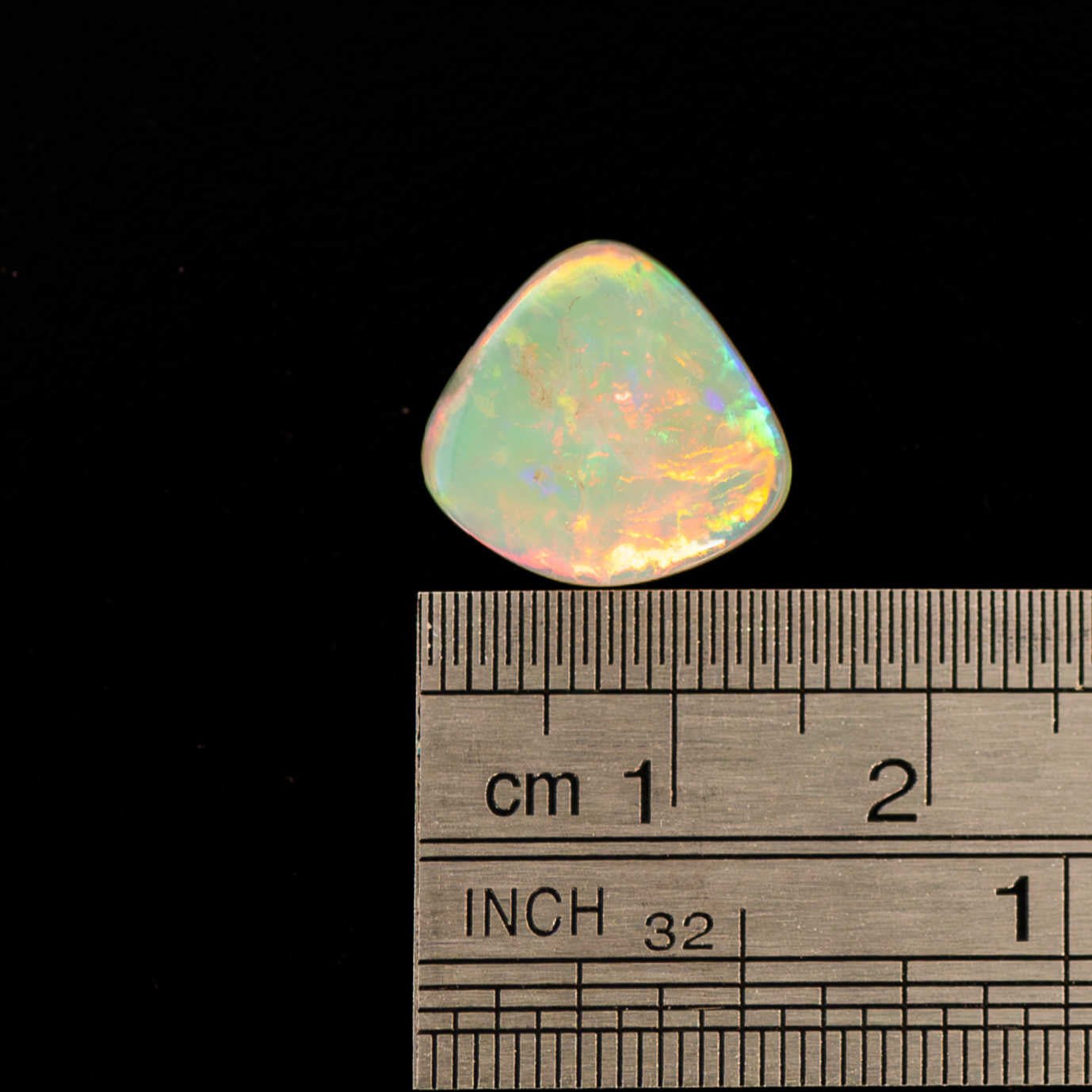 Australian opal stone with a ruler for scale on a black background