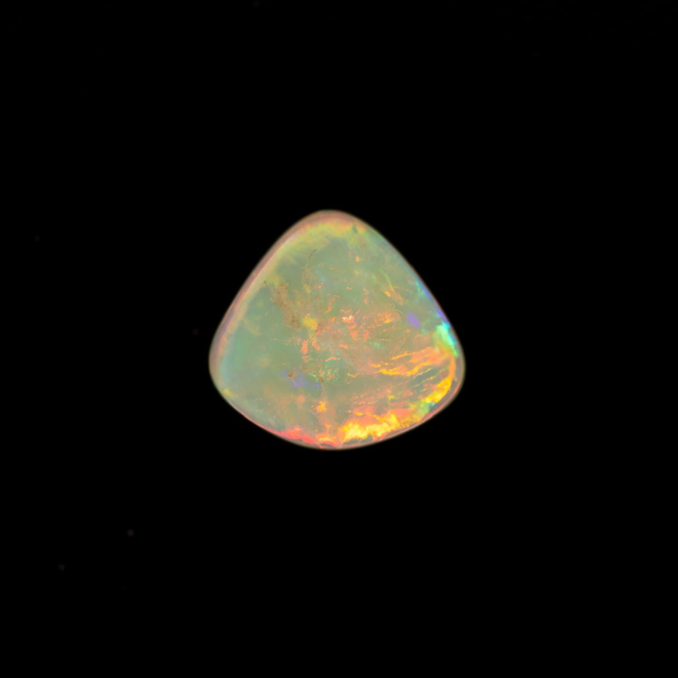 Triangular opal stone with multicolored play of light on a black background
