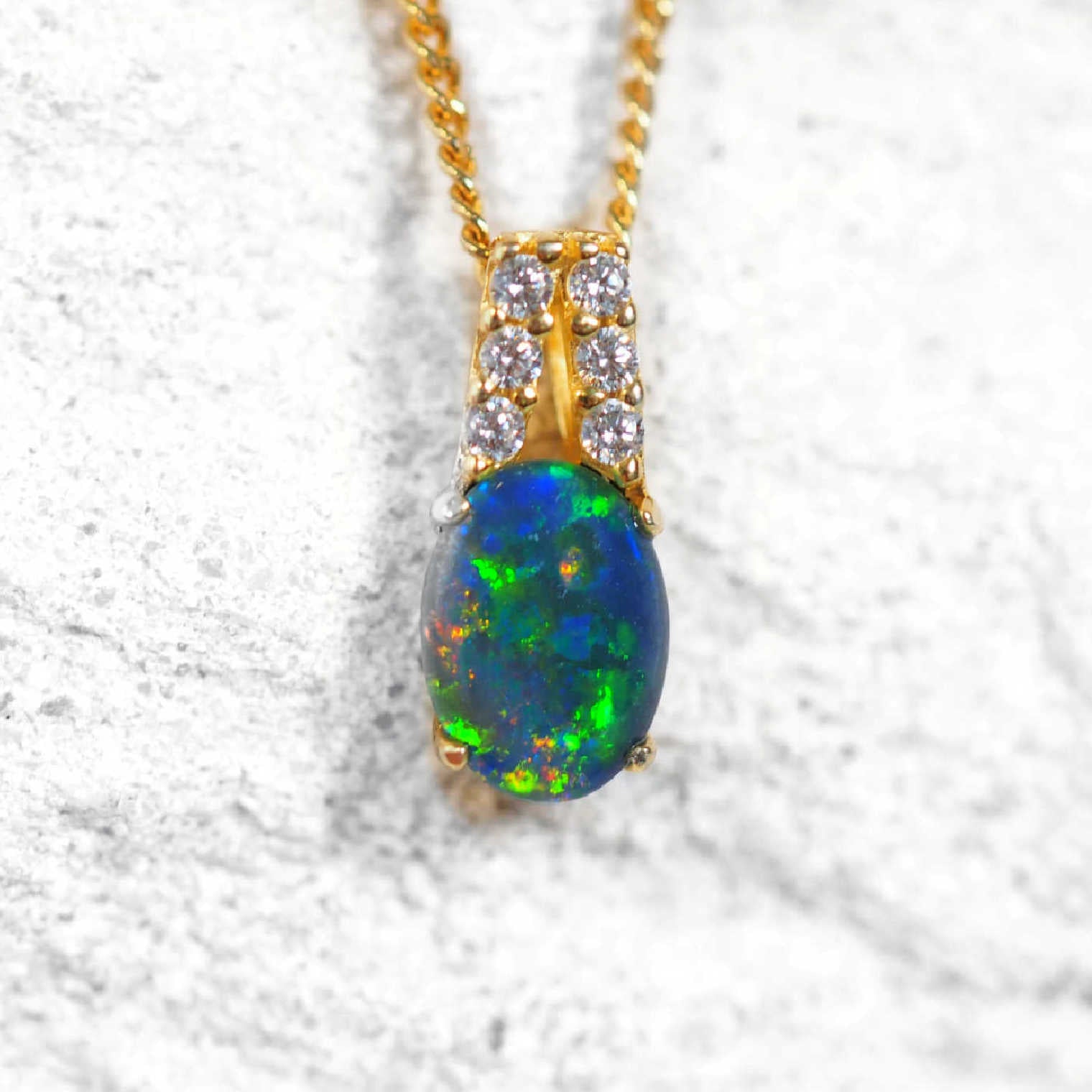 Colourful opal pendant with gold chain on a textured white background