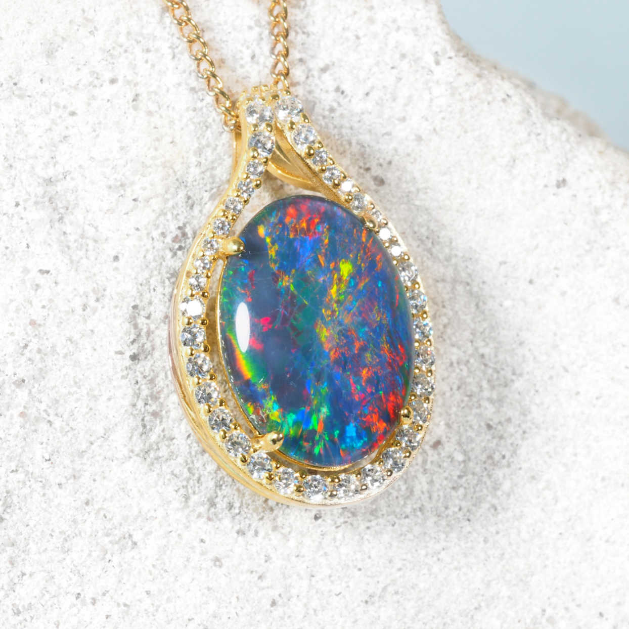 Opal pendant necklace with gold frame and gemstones on a textured surface