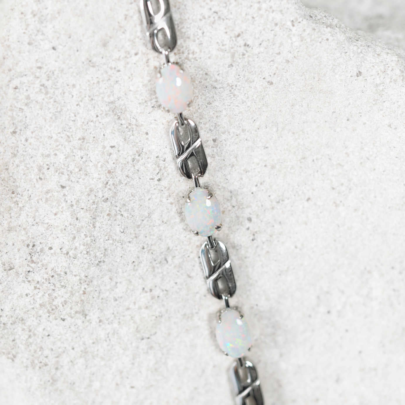 Bracelet with opal beads and silver links on a white sand background