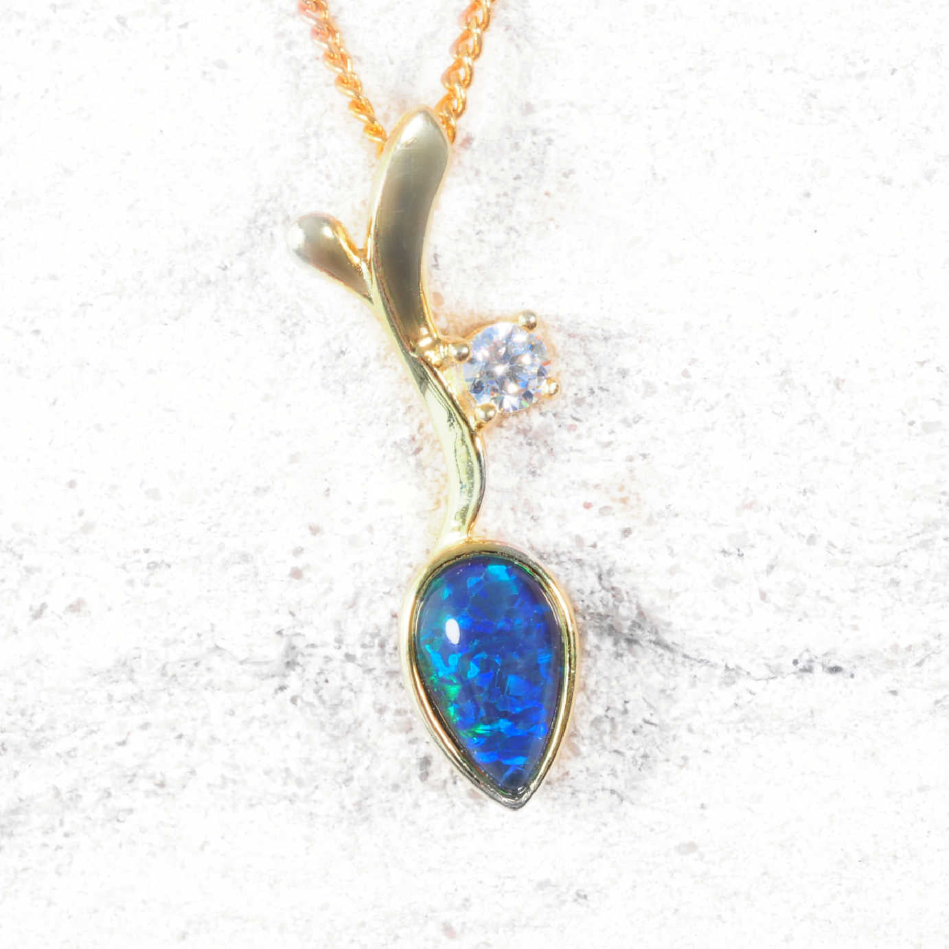 Gold opal pendant with a blue gemstone on a white background