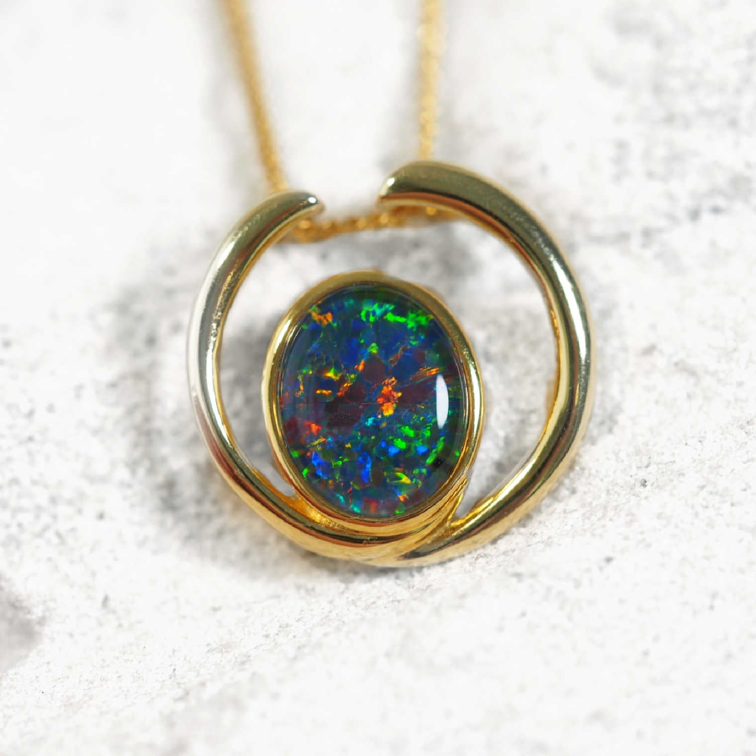 Gold pendant with a colorful opal gemstone on a white background
