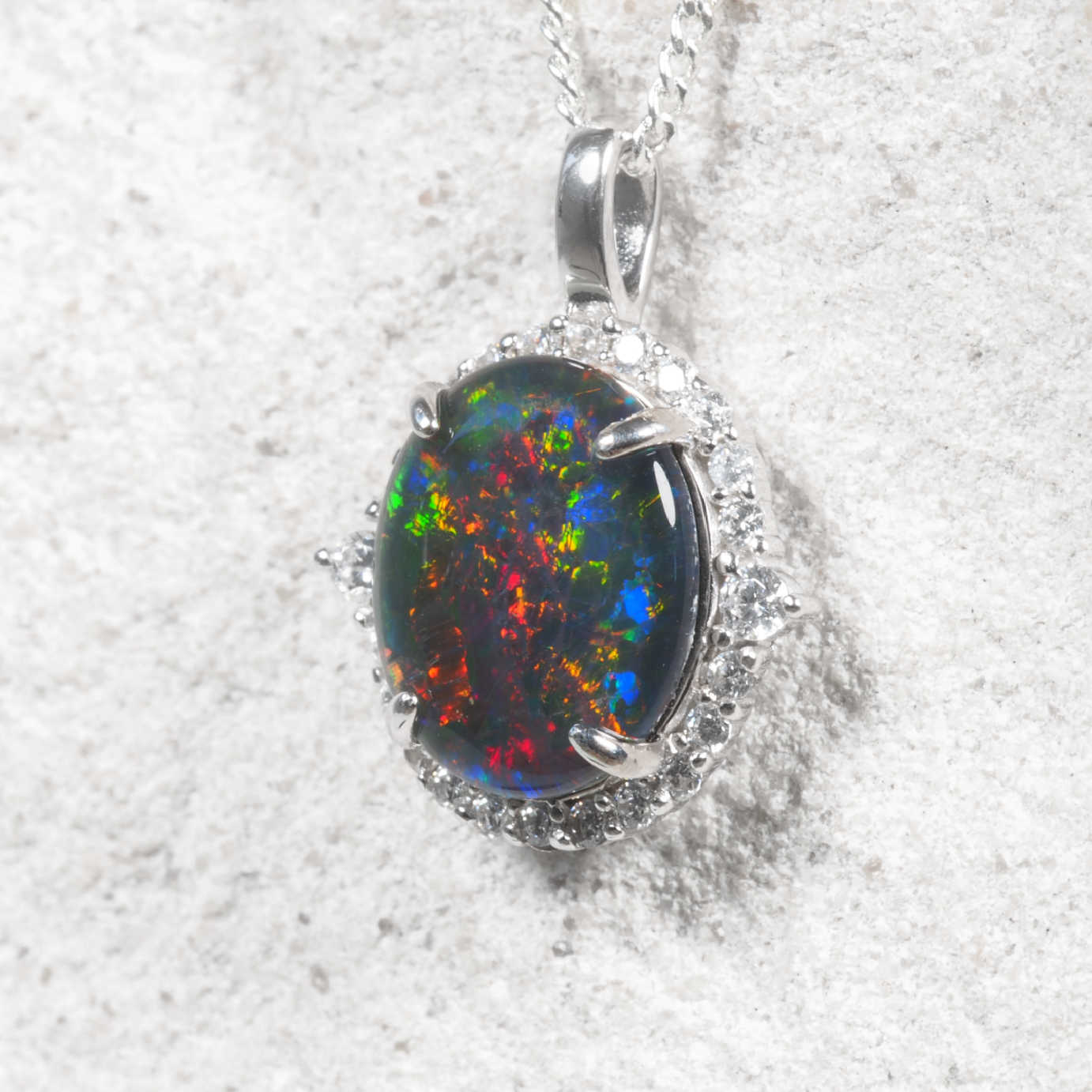 An oval Australian opal pendant in sterling silver with brilliant red, green and blue natural play-of-colour, accented by a halo of sparkling cubic zirconias