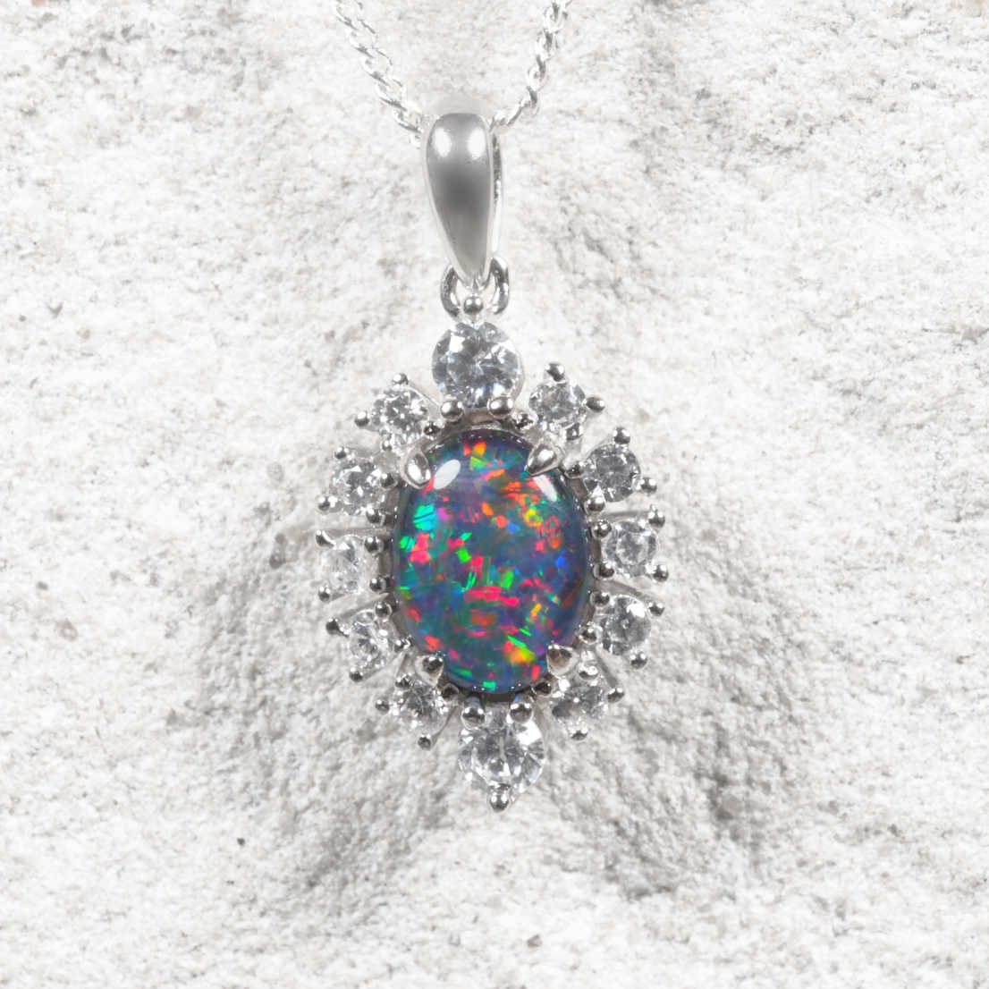 Australian triplet opal necklace in polished sterling silver with an oval claw-set opal displaying brilliant blue, green, red and golden flashes, surrounded by twelve cubic zirconias.