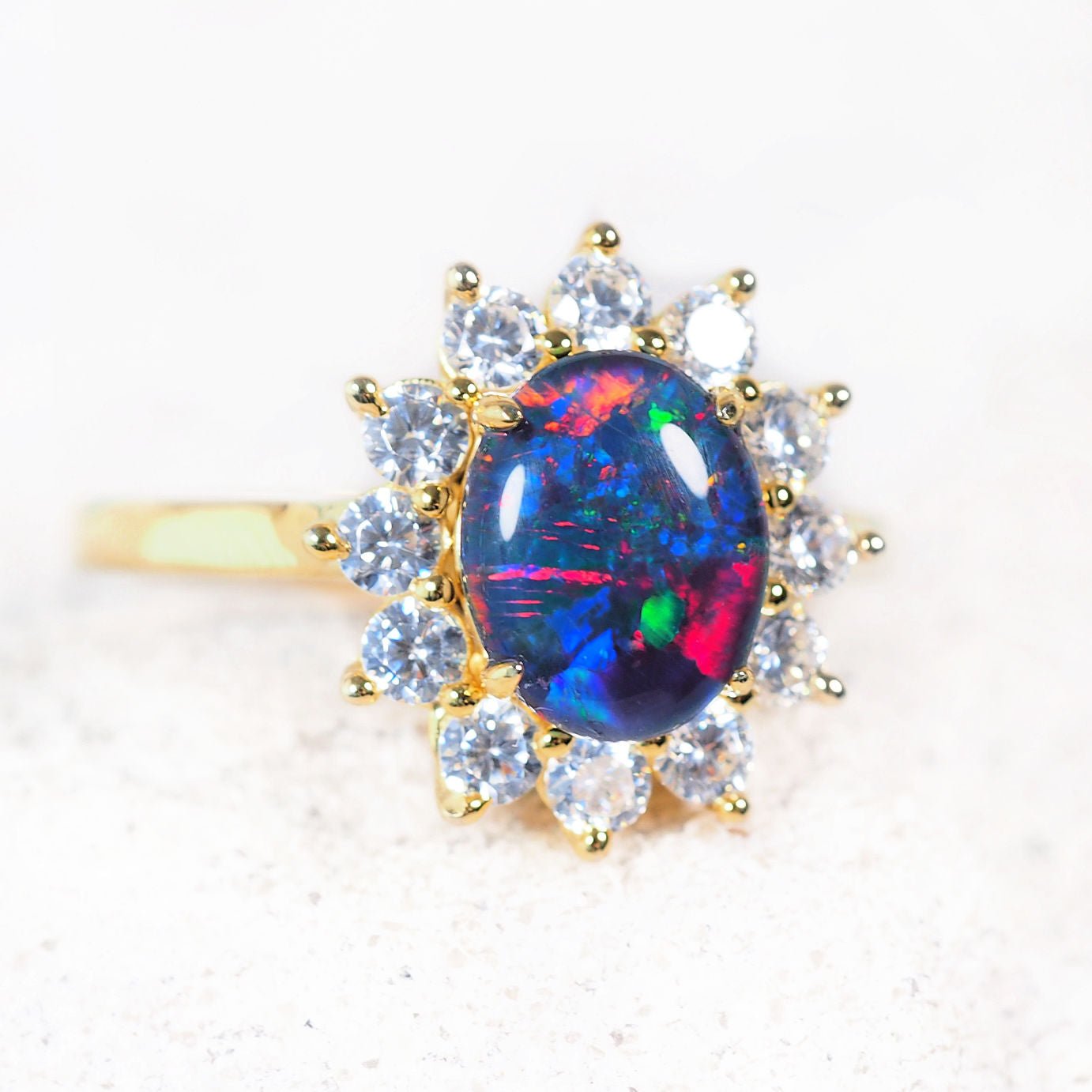 Gold coloured ring with a colorful opal gemstone and diamond-like stones