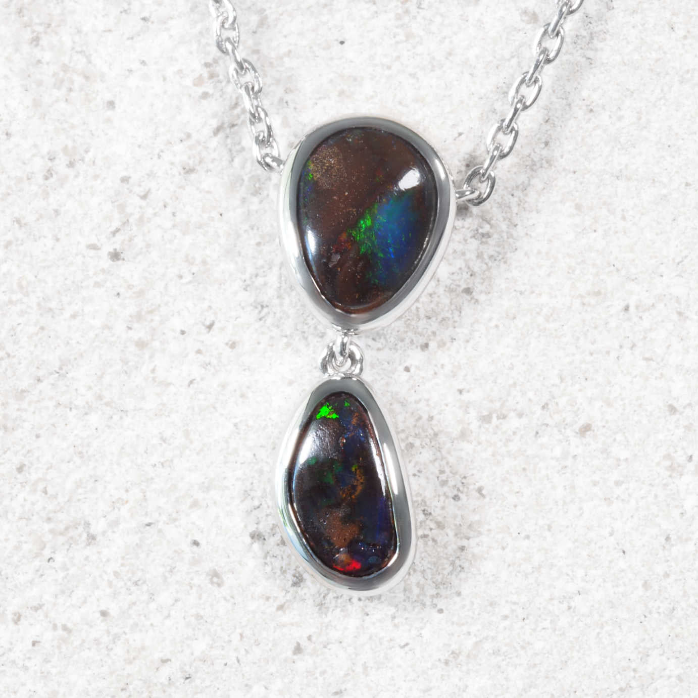 Queensland opal necklace with two opal stones in silver setting on a textured white background