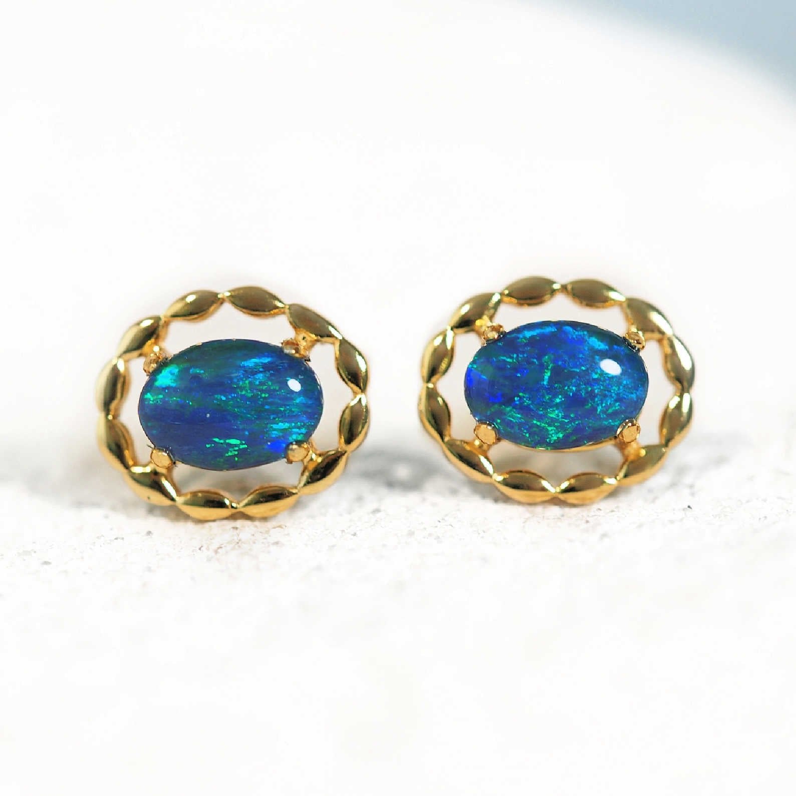 Pair of gold-framed blue opal earrings on a white background