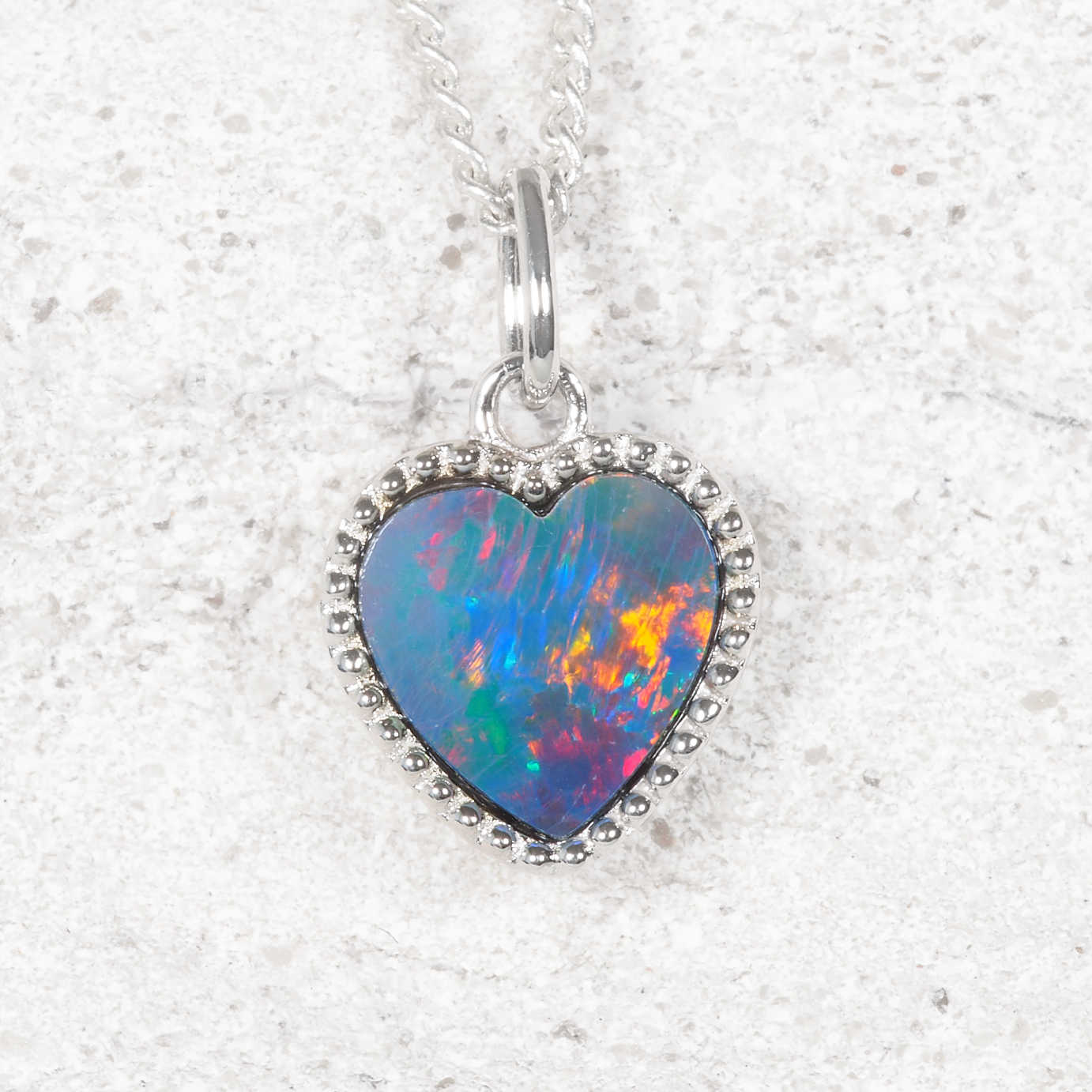 Heart-shaped opal pendant with silver frame on a textured white background