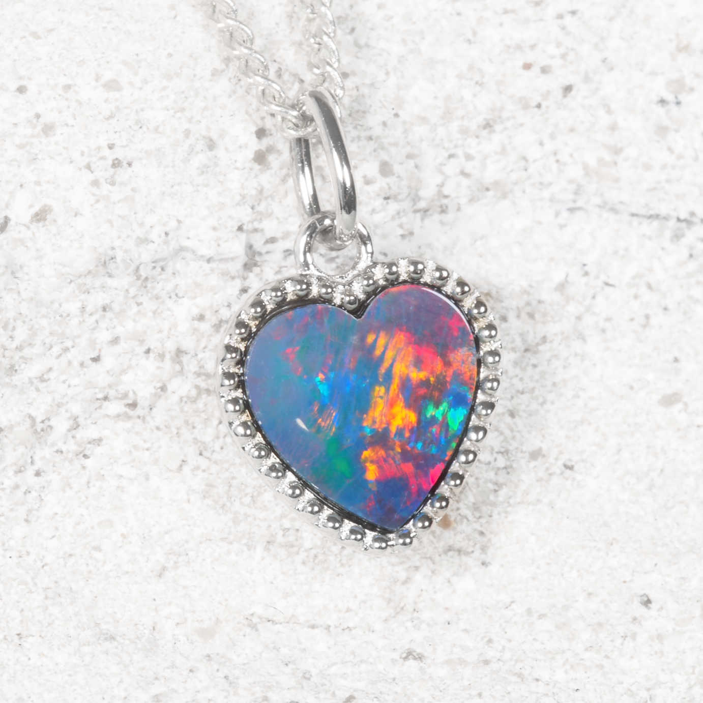 Heart-shaped opal pendant on a silver chain against a textured white background