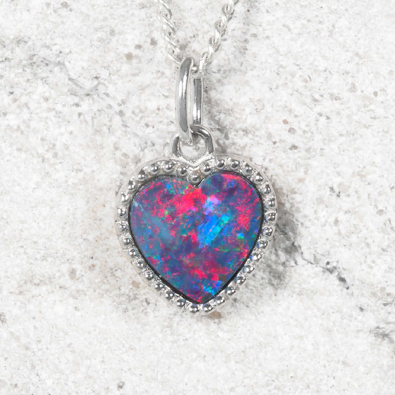 Heart-shaped opal pendant on a silver chain against a textured white background