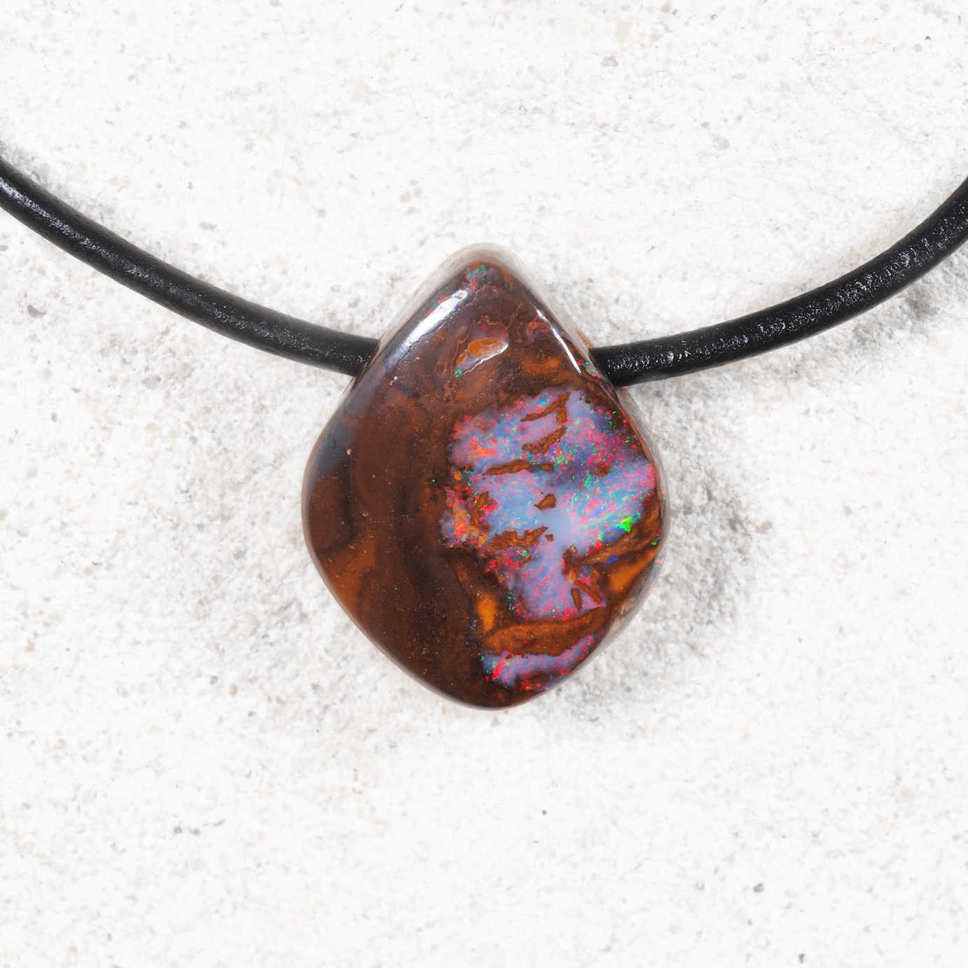 Necklace with a large, colorful opal stone on a white sandy background
