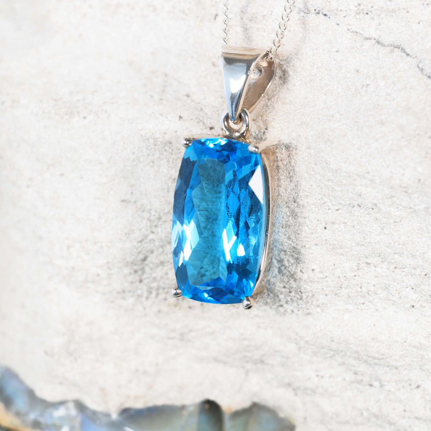 Close-up of the 'Jamie' pendant highlighting faceted light Blue Topaz set in a polished claw silver frame