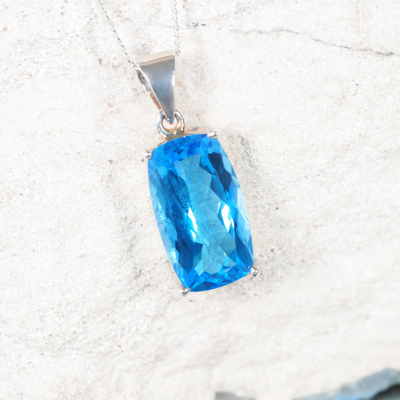 The 'Jamie' light Blue Topaz pendant in a claw-style silver bezel, showing a faceted rectangular gemstone with sparkling blue hues