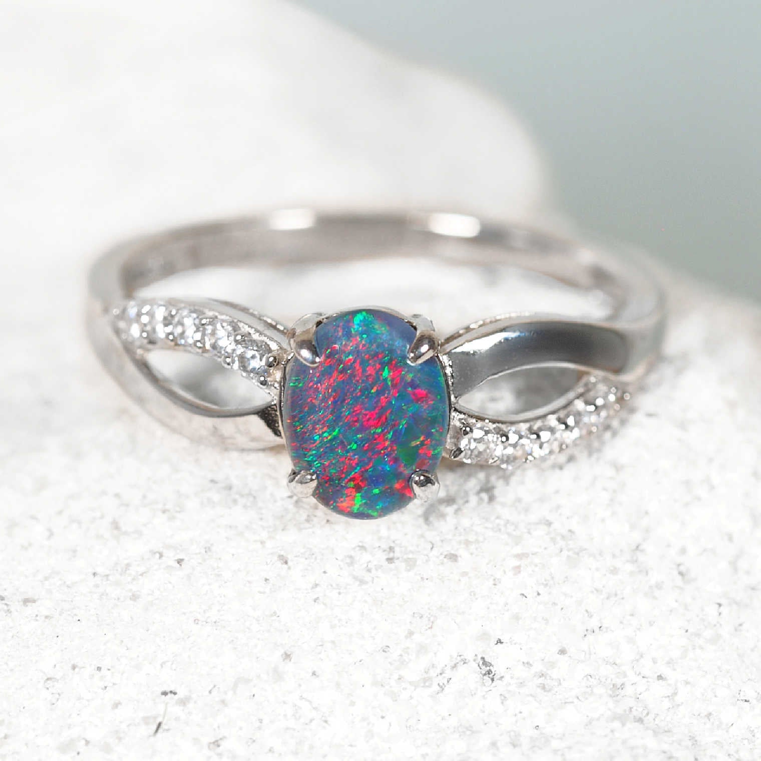 Silver ring with a colorful opal stone on a light gray background
