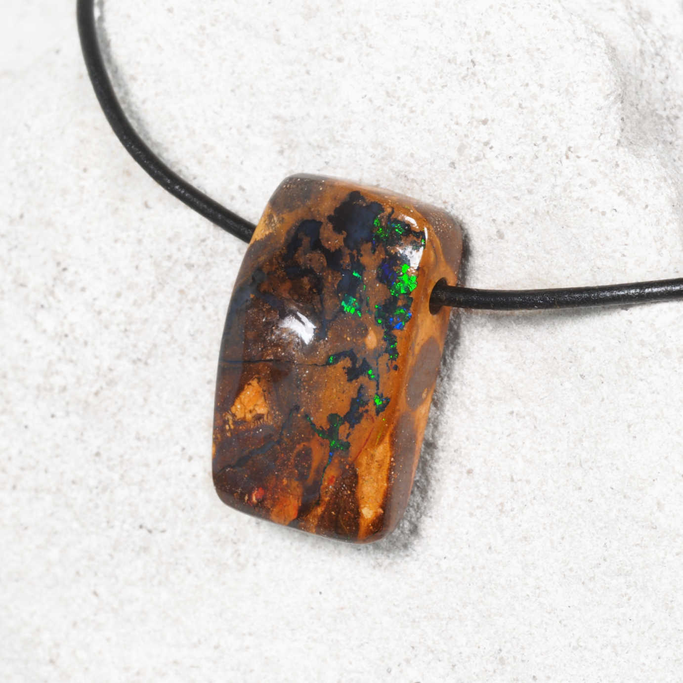Opal pendant on a black cord against a white background