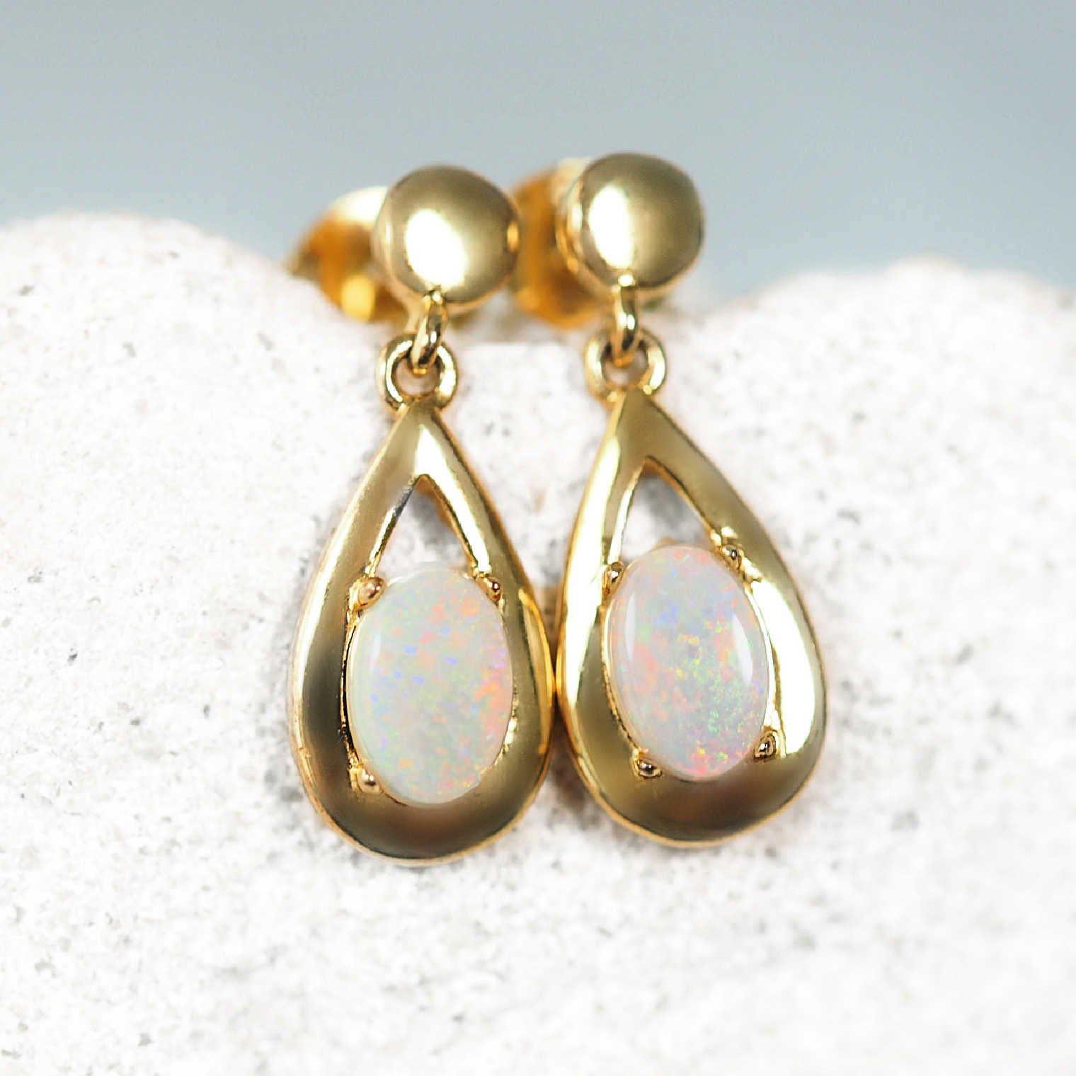 Gold earrings with opal stones on a textured surface